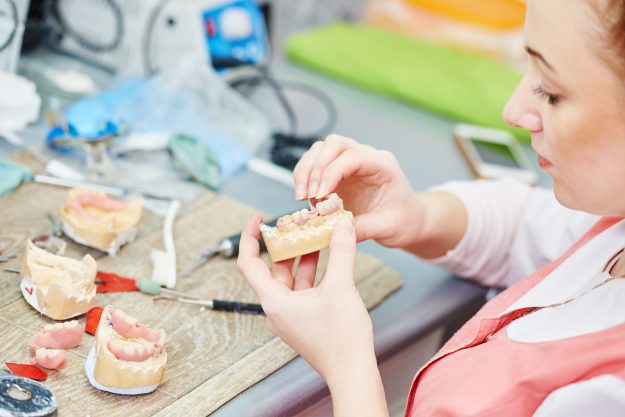 Dental technician working with tooth dentures at prosthesis labo